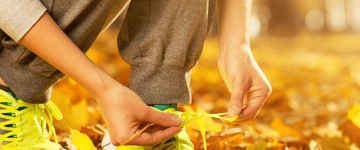 Photo of a woman tying her shoelaces surrounded by autumn leaves