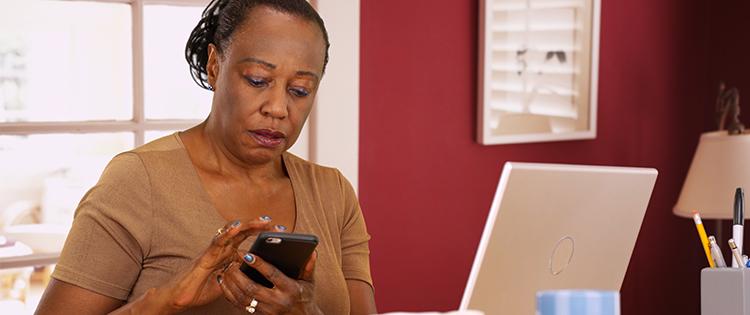 Photo of a middle aged black woman looking at her smartphone while sitting at her desk