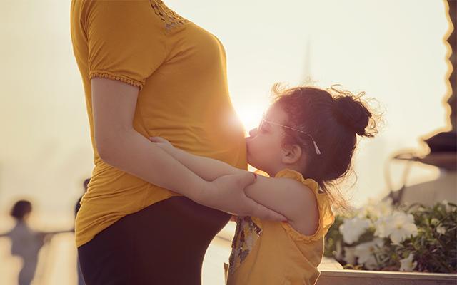 Photo of a young girl kissing her mother's pregnant stomach
