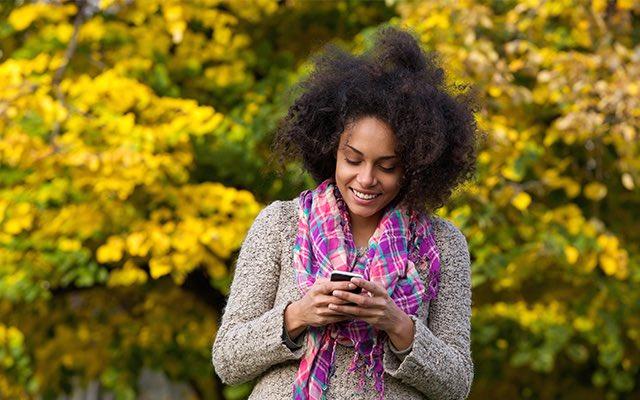 Photo of a young black woman looking at her smartphone outside