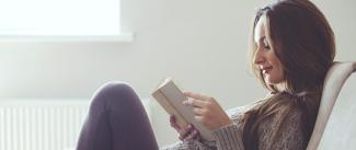 Photo of a dark haired woman reading a book on the couch