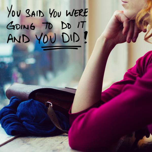 A young woman looks out a window onto a street. Her satchel bag and sweater sit in a pile on the counter top to her side. Text reads "You said you were going to do it and you did!"