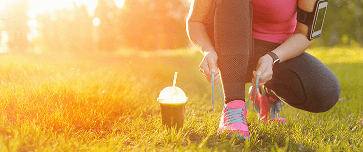 Photo of a woman in workout clothing kneeling to tie her running shoes