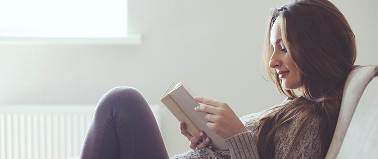 Photo of a dark haired woman reading a book on the couch