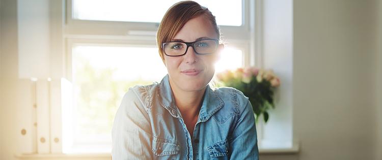 Photo of a women wearing glasses sitting in front of a window in her home