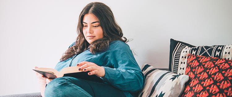 Photo of a dark haired woman reading a book on the couch