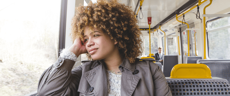 Photo of a young black woman commuting on a train and looking out the window.