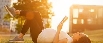 Photo of a pregnant woman reading a book while lying in the grass