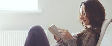 Photo of a dark haired woman reading a book on the couch