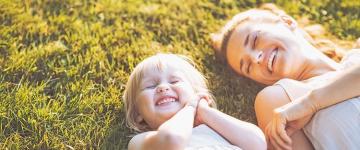 Photo a mother and her toddler smiling and laying on the grass outside