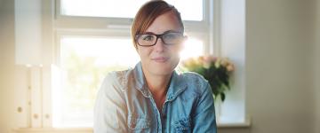 Photo of a women wearing glasses sitting in front of a window in her home