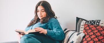 Photo of a dark haired woman reading a book on the couch