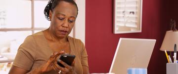 Photo of a middle aged black woman looking at her smartphone while sitting at her desk