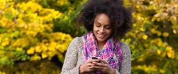 Photo of a young black woman looking at her smartphone outside