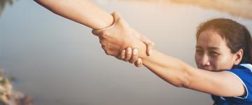 Photo of a woman grabbing someone's arm to help her climb a mountain