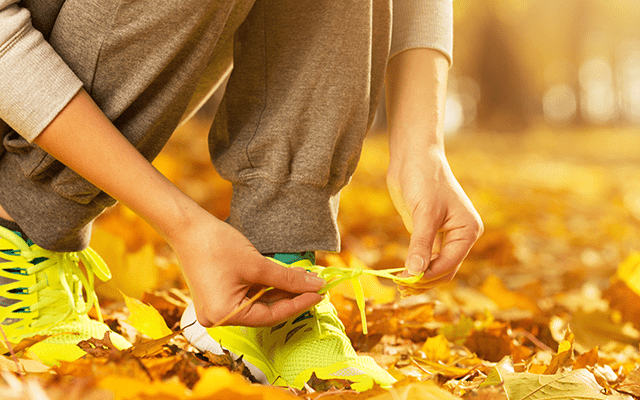 Photo of a woman tying her shoelaces surrounded by autumn leaves