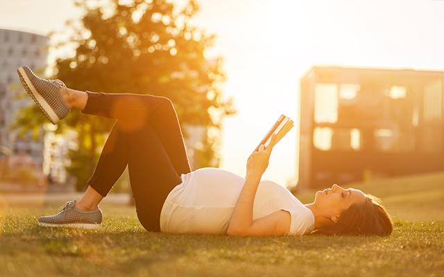 Photo of a pregnant woman reading a book while lying in the grass