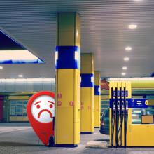 An animated red location marker, like one on a map, that has a frowning face, is looking out from behind a column at a gas station pump.