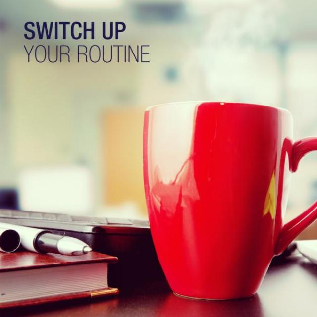 A red coffee cup sits on a desk crowded with books. In the top corner it reads "Switch up your routine."