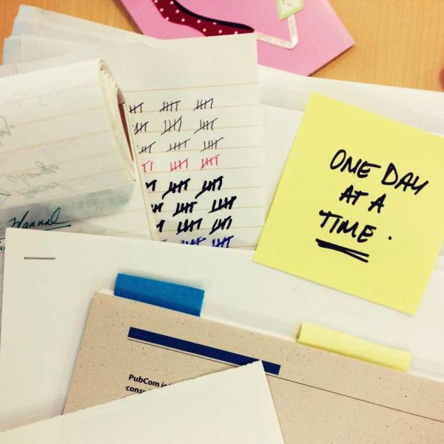 Photo of a pile of papers with a post-it note saying "One day at a time."